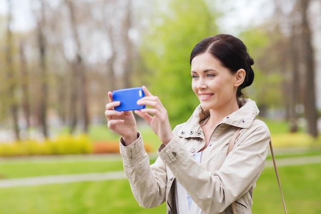 bebidas, lazer, tecnologia e conceito de pessoas - mulher sorridente tirando foto com smartphone no parque