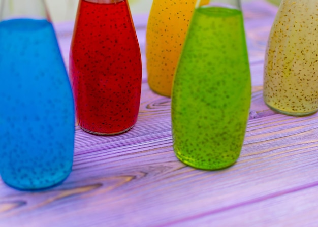 Bebidas multicolores con semillas en botellas sobre un fondo de madera violeta