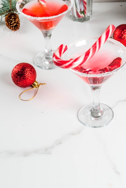 Bebidas navideñas, cóctel de martini de menta rosa con decoración de Navidad y bastón de caramelo dulce en mesa de cocina de mármol blanco, copyspace