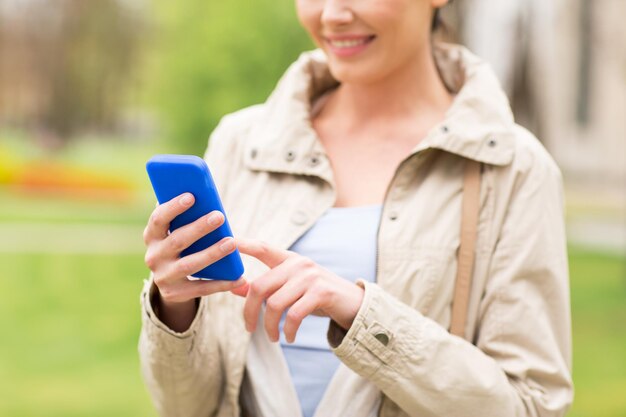 bebidas, ocio, tecnología y concepto de personas - mujer sonriente llamando o enviando mensajes de texto en un teléfono inteligente en el parque