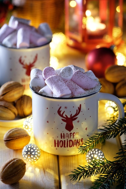 Bebidas quentes de Natal com marshmallows na mesa com nozes, árvore de Natal e luzes