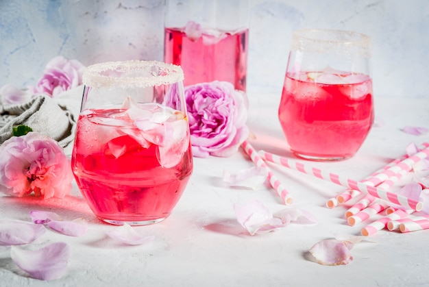 Foto bebidas refrescantes de verão coquetel rosa claro com vinho rosé chá pétalas de limão em uma mesa de concreto de pedra branca com túbulos listrados rosa pétalas e flores rosas