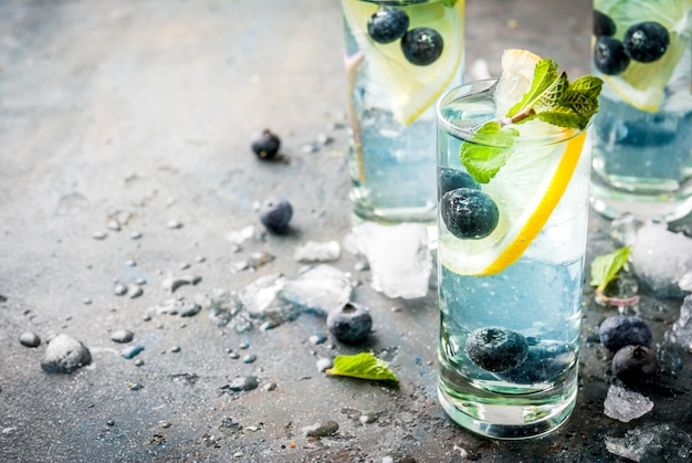 Bebidas refrescantes de verano, limonada de arándanos o cóctel de mojito con limón, arándanos frescos y menta, copyspace de piedra azul oscuro