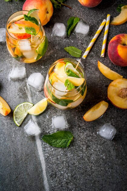 Bebidas refrescantes de verano. Mojito de durazno con lima, durazno y menta. Con los ingredientes en una mesa de piedra oscura. vista superior