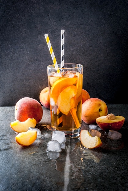 Bebidas refrescantes de verano. Té helado con trozos de melocotón casero orgánico de nectarina. Sobre un fondo de piedra negra, con hielo e ingredientes. copyspace