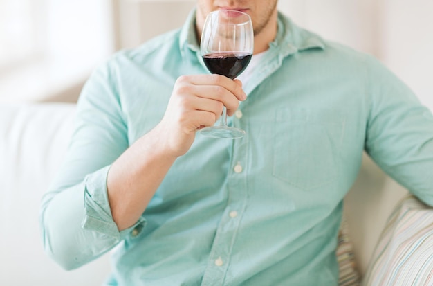 bebidas, relax, ocio y concepto de la gente - cerca de un hombre bebiendo vino tinto y sentado en el sofá en casa