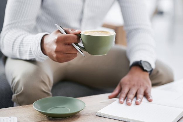 Bebiendo café mientras trabaja en sus grandes planes Captura de pantalla de un hombre de negocios irreconocible tomando café mientras escribe notas en una oficina