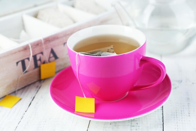 Becher mit Teekanne und Teebeuteln auf Holztisch in der Nähe