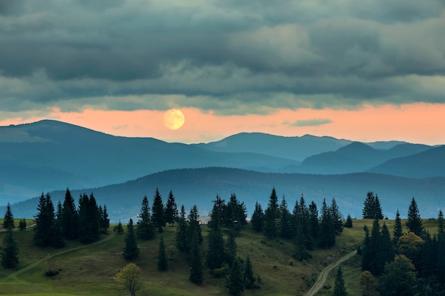 Bedeckt mit Nebelbergen bei Mondaufgang, großer Mond auf hellem orange Himmel über hohem