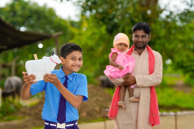 Bedeutung des Sparkonzepts: Intelligenter indischer kleiner Junge, der mit seinem Vater und seiner kleinen Schwester ein Sparschwein in der Hand steht und hält.