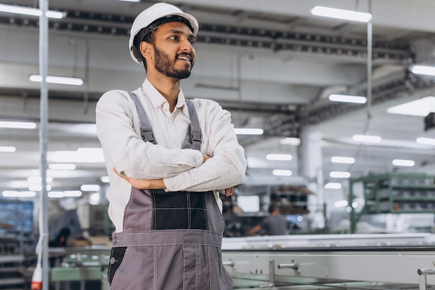 Bediener der Maschine. Industrieller indischer internationaler Arbeiter drinnen in der Fabrik. Junger Techniker mit weißem Schutzhelm