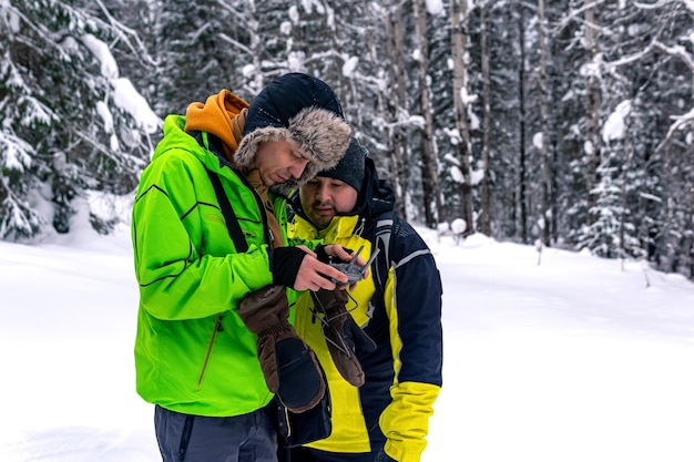 Bediener mit Assistent steht in einem Winterwald und steuert eine Luftdrohne