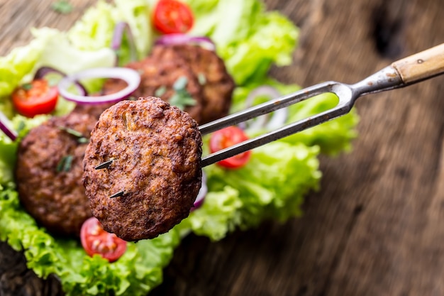 Beef Burger Frikadellen Koteletts mit Salat Salat Tomaten Zwiebeln auf Holzbrett.