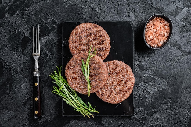 Beef Burger Patty Schnitzel für Hamburger gegrillt auf BBQ auf Marmorplatte mit Rosmarin Schwarzer Hintergrund Draufsicht