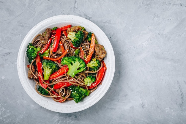 Beef Noodle Stir Fry mit Brokkoli, Karotten und roten Paprikaschoten auf grauem Steinhintergrund