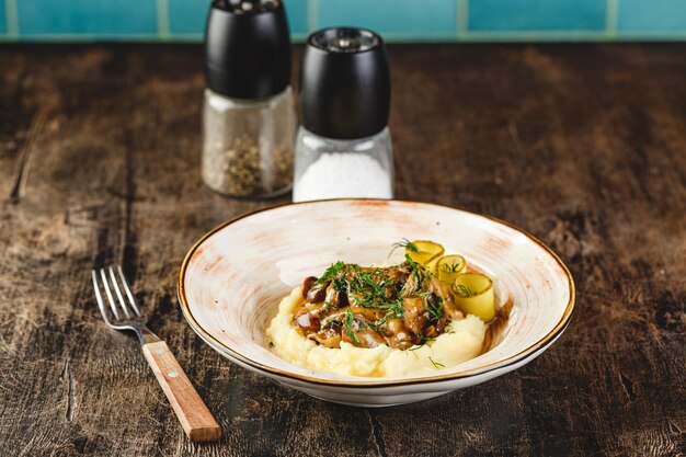 Beef Stroganoff mit Kartoffelpüree und eingelegten Gurkenscheiben in Platte auf Holztisch im Café