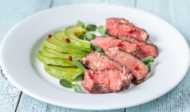 Beefsteak mit rotem Pfefferkorn dekoriert und mit Avocado-Scheiben garniert