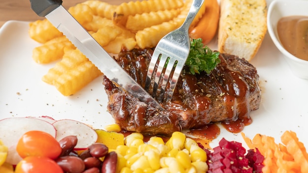 Beefsteak, Pommes Frites und Gemüse auf einem weißen Teller.