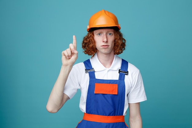 Beeindruckt zeigt auf jungen baumeister mann in uniform isoliert auf blauem hintergrund