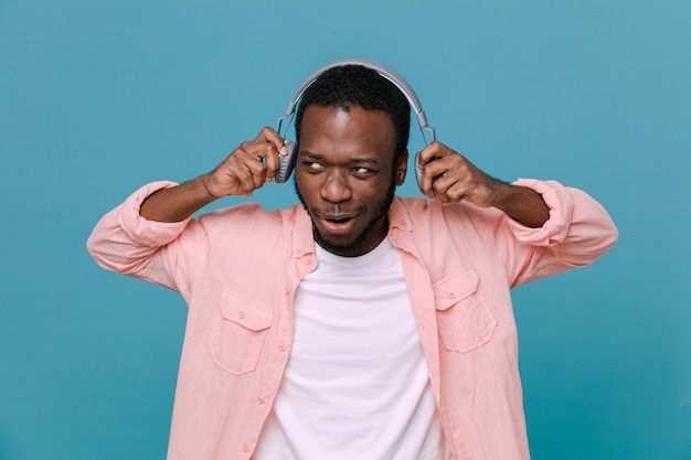 Beeindruckter junger Afroamerikaner mit Kopfhörern isoliert auf blauem Hintergrund