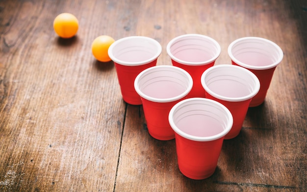 Beer pong Copos de cor vermelha de plástico e bolas de pingue-pongue em fundo de madeira