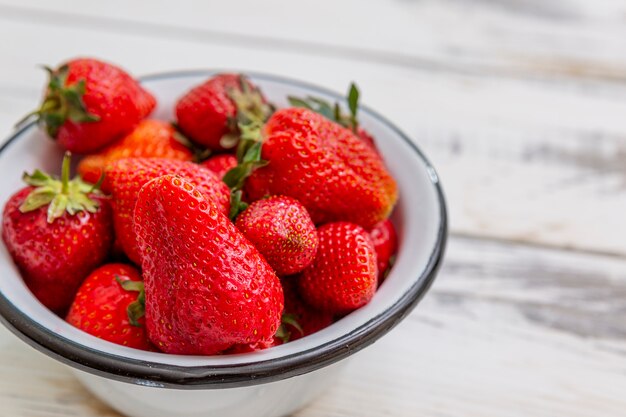 Beeren der reifen roten Erdbeeren in einer Schüssel auf einem hellen hölzernen Hintergrund. Saisonale Vitamine. Nahansicht. Draufsicht.