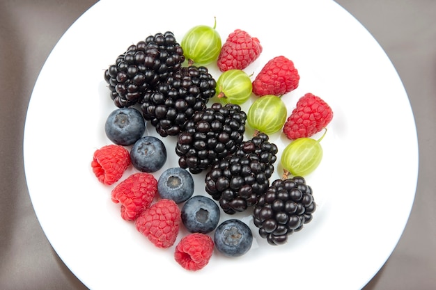 Beeren Himbeeren, Blaubeeren, Stachelbeeren und Brombeeren auf einem weißen Teller. gesundes Essen Obst. gesundes Gemüsefrühstück