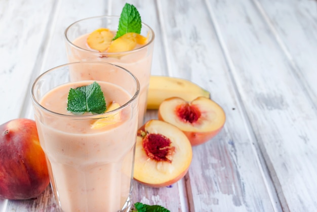 Beeren-Smoothies von Aprikose, Pfirsich und Banane in Gläsern und Zutaten auf einem Holztisch