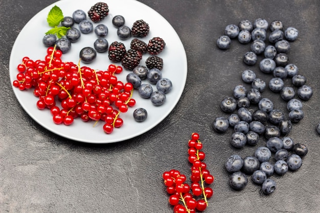 Beeren von reifen roten Johannisbeeren Brombeeren und Heidelbeeren auf grauem Teller und auf dem Tisch