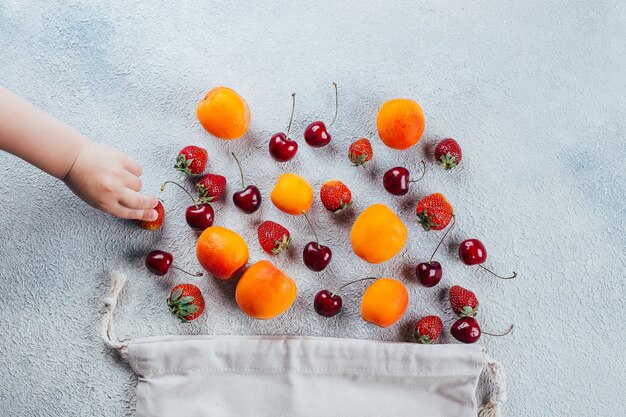 Beerenerdbeere, Kirsche und Aprikose. Babyhand nimmt Beere.