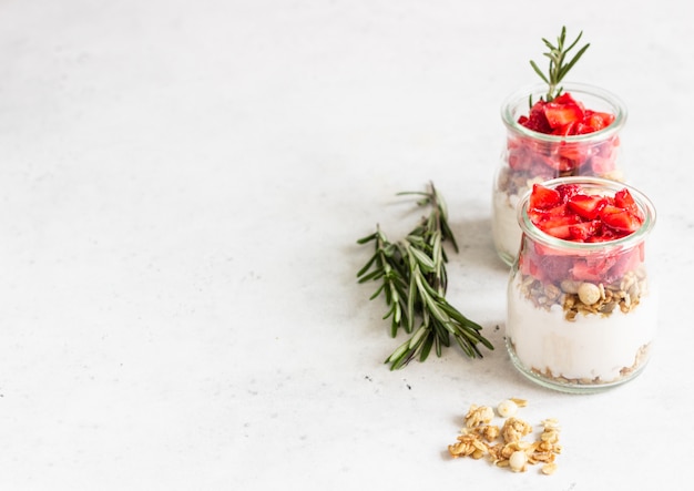 Beerenjoghurt mit griechischem Joghurt, frischen Erdbeeren und Müsli in Gläsern. Gesundes Frühstücksparfait in der Glasschale