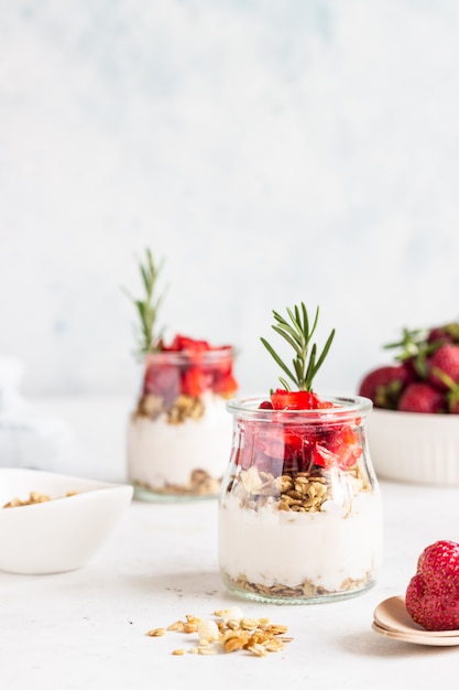 Beerenjoghurt mit griechischem Joghurt, frischen Erdbeeren und Müsli in Gläsern. Gesundes Frühstücksparfait in der Glasschale