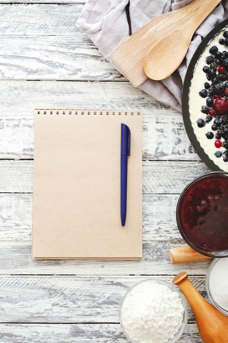 Foto beerenkuchen mit kirsche, johannisbeere, brombeere, blaubeere mit küchengeschirr und rezeptmodell auf weißem holztisch. käsekuchen draufsicht modell