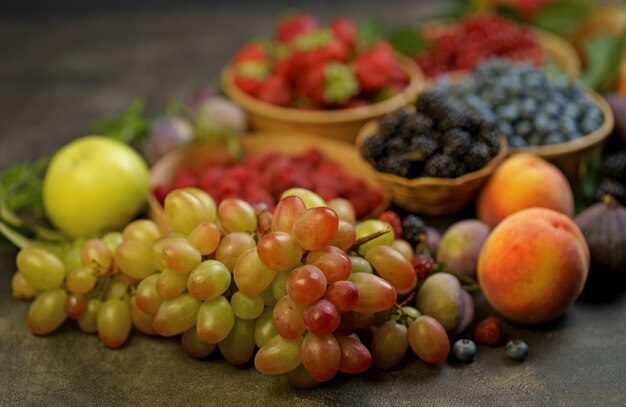 Beerenmischung Eine Vielzahl von Sommerbeeren, Trauben, Himbeeren, Erdbeeren, Heidelbeeren, Kirschen, Johannisbeeren, Pflaumen in Tassen auf einem Holztisch