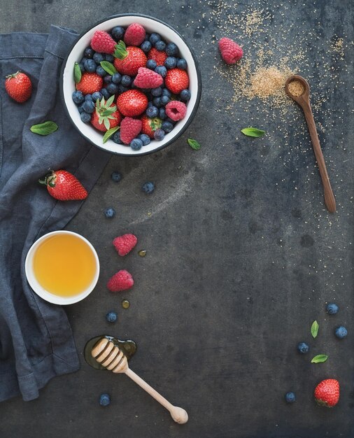 Beerenrahmen mit Kopierbereich auf der rechten Seite Erdbeeren, Himbeeren, Heidelbeeren und Minzblätter, dunkler Grunge-Hintergrund