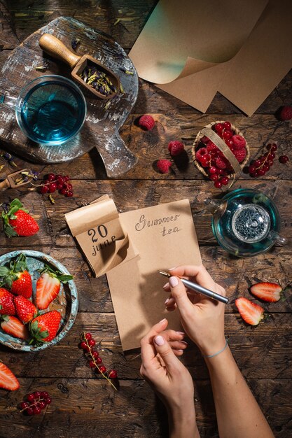 Beerenstillleben. Beeren, Tee, Stift, Kalender, Notizbuch auf einem alten braunen Holztisch, Draufsicht