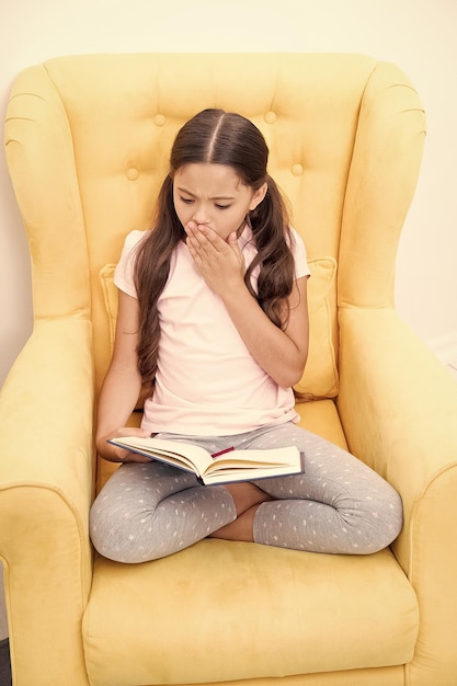 Begeistert von spannender Geschichte Lesehobby Mädchen Kind sitzen gelben Sessel Buch lesen Kind süßer Bücherwurm Mädchen Kind süßer Pyjama entspannen Märchenbuch lesen vor dem Schlafen Nützliche Gewohnheiten fördern