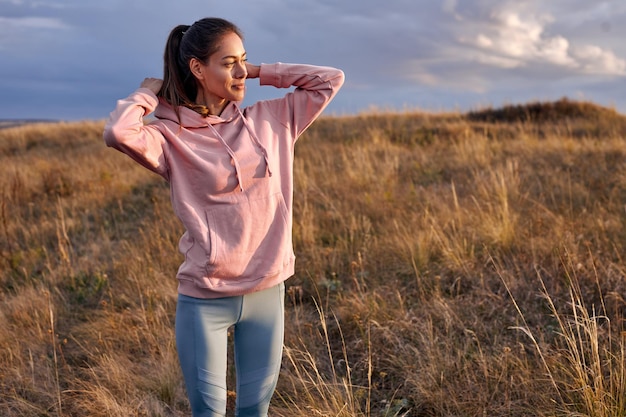 Begeisterte Dame trägt Hoodie-Kapuze und schaut bei Sonnenuntergang oder Sonnenaufgang zur Seite