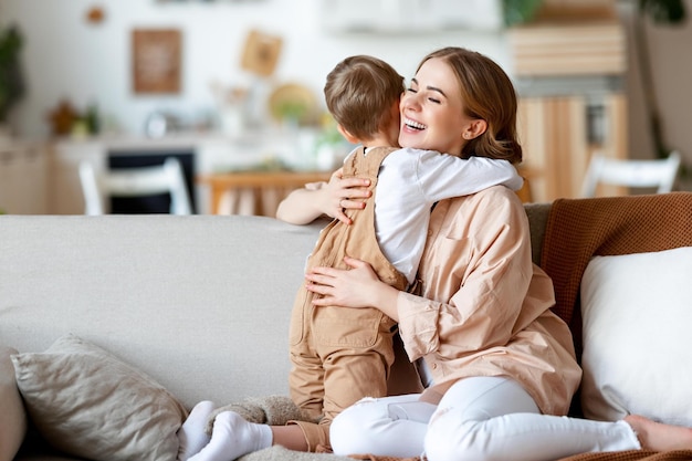 Begeisterte erwachsene Frau, die den Jungen lächelt und umarmt, während sie sich zu Hause auf der Couch ausruht