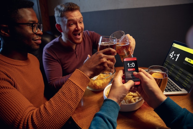 Begeisterte Fans in der Bar mit Bier und mobiler App zum Wettergebnis auf ihren Geräten