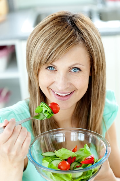 Begeisterte Frau, die einen Salat in der Küche isst