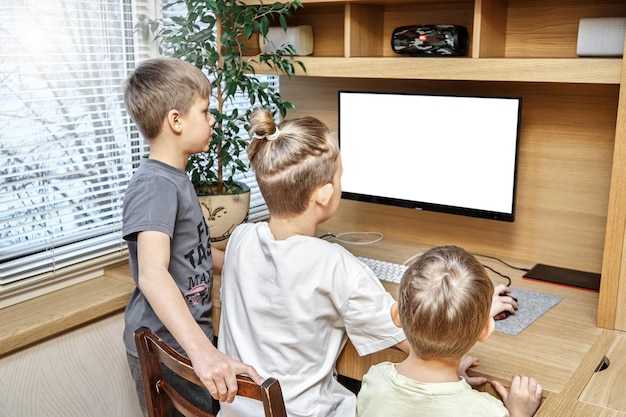 Begeisterte Kinder sitzen auf einem Stuhl in der Nähe eines braunen Computertisches aus Holz und schauen in ein weißes Display