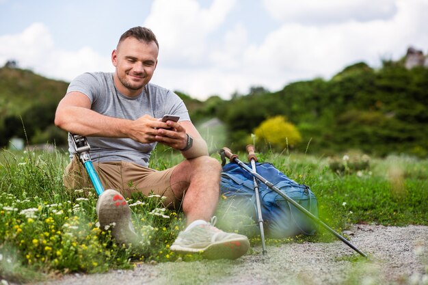 Begeisterter junger Mann mit Behinderung, der sein Telefon benutzt, während er sich auf dem Gras ausruht