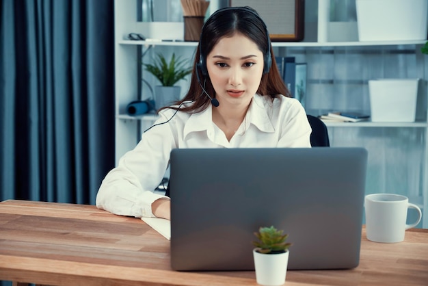 Begeistertes asiatisches Callcenter mit Headset und Mikrofon, das an ihrem Laptop arbeitet