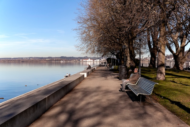 Foto begenz / áustria - janeiro de 2020: as pessoas estão relaxando em bancos e caminhando ao longo do calçadão do lago constança (bodensee) em bregenz.