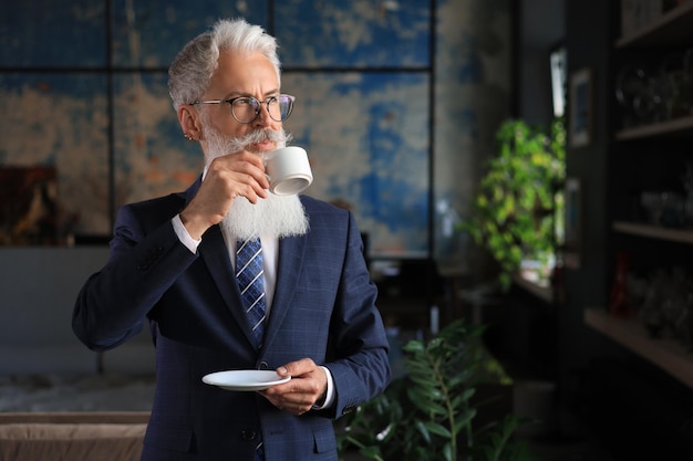 Beginn eines neuen Arbeitstages mit einer Tasse Kaffee Schöner reifer Mann mit Kaffeetasse in seinem modernen Büro