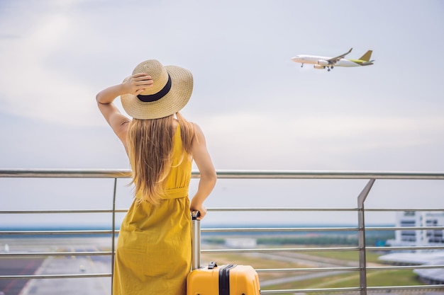 Beginn ihrer Reise Schöne junge Frau ltraveler in einem gelben Kleid und einem gelben Koffer wartet auf ihren Flug