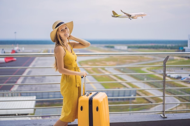 Beginn ihrer Reise Schöne junge Frau ltraveler in einem gelben Kleid und einem gelben Koffer wartet auf ihren Flug