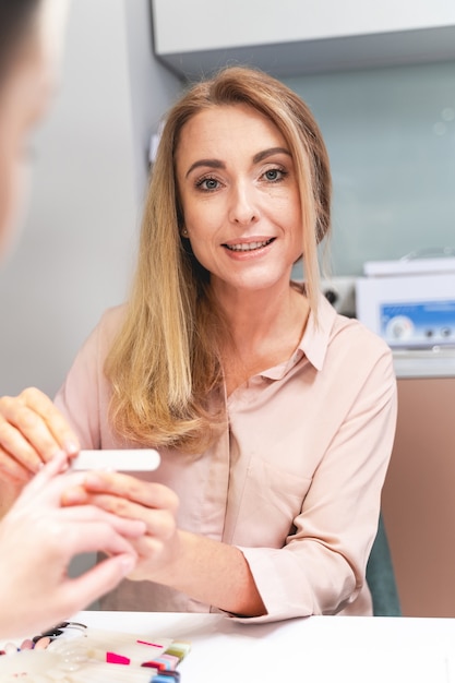 Begleiten Sie uns. Begeisterte junge Frau, die bei der professionellen Maniküre ein Lächeln auf ihrem Gesicht hält. Schönheitskonzept