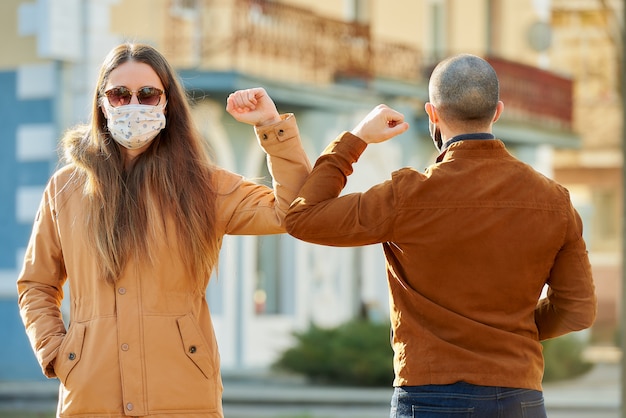 Begrüßung des Ellenbogens, um die Ausbreitung des Coronavirus (COVID-19) zu vermeiden. Ein Mann und eine Frau in medizinischen Gesichtsmasken treffen sich mit bloßen Händen auf der Straße. Anstatt mit einer Umarmung oder einem Händedruck zu grüßen, stoßen sie an die Ellbogen.